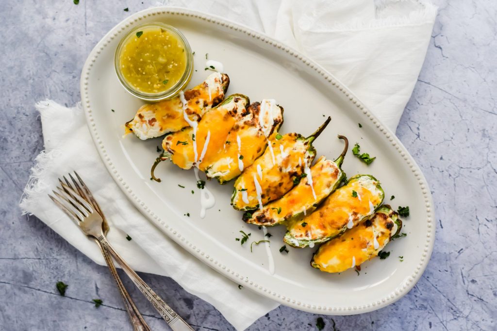 tray of air fried jalapeno poppers topped with cheese, mexican crema, and salsa verde