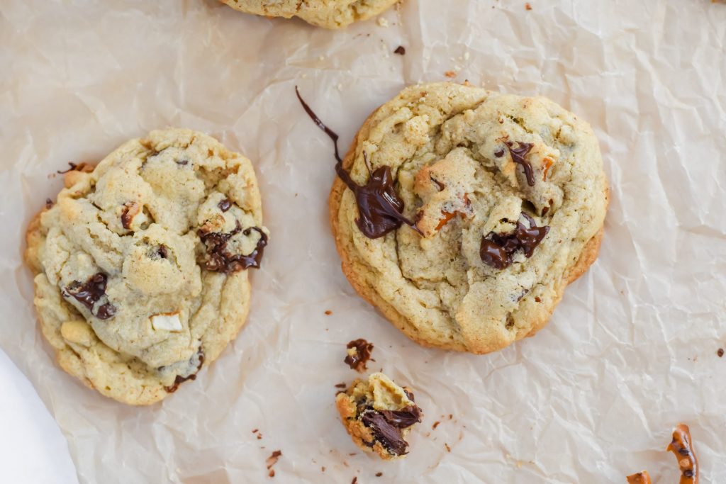 two chocolate chip pretzel peanut butter cookies on parchment with oozing chocolate chips 