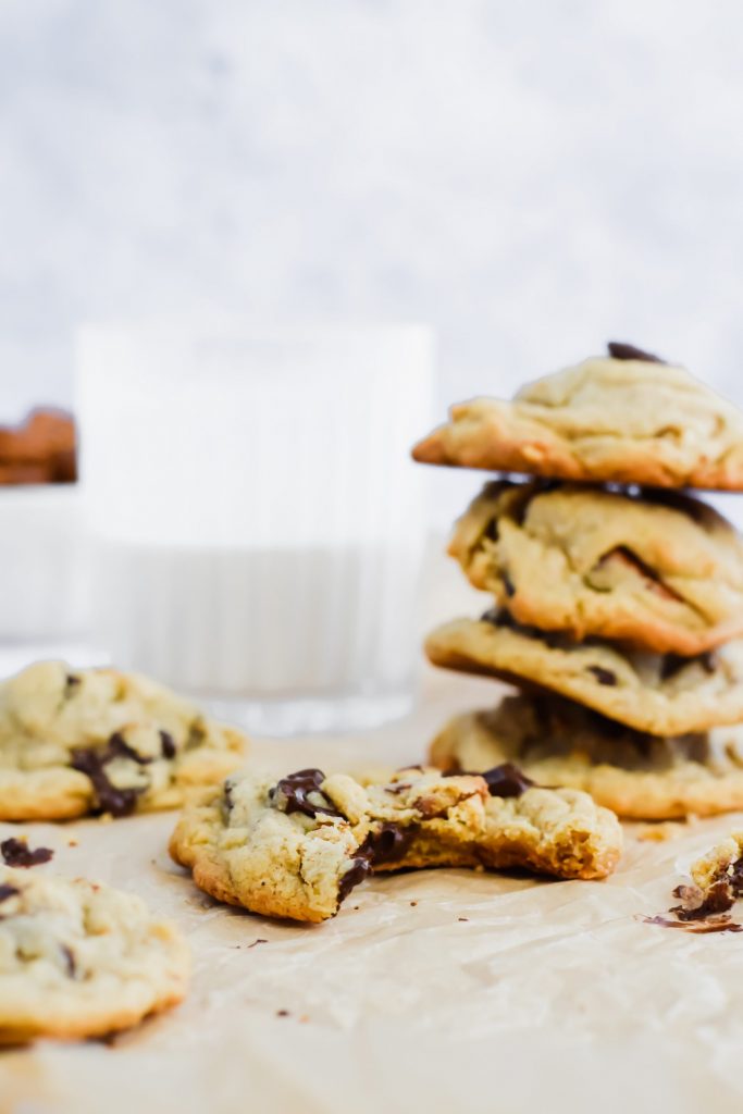 stacked chocolate chip pretzel peanut butter cookies along side one cookie with a bite taken out of it on parchment