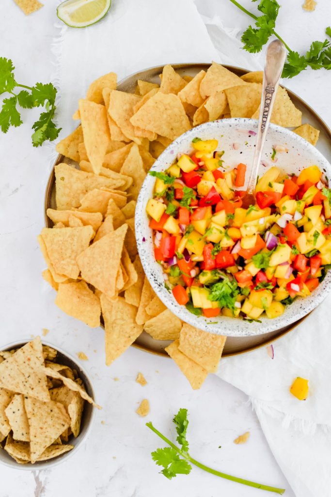 ceramic bowl filled with fresh mango salsa and chips with greenery around it