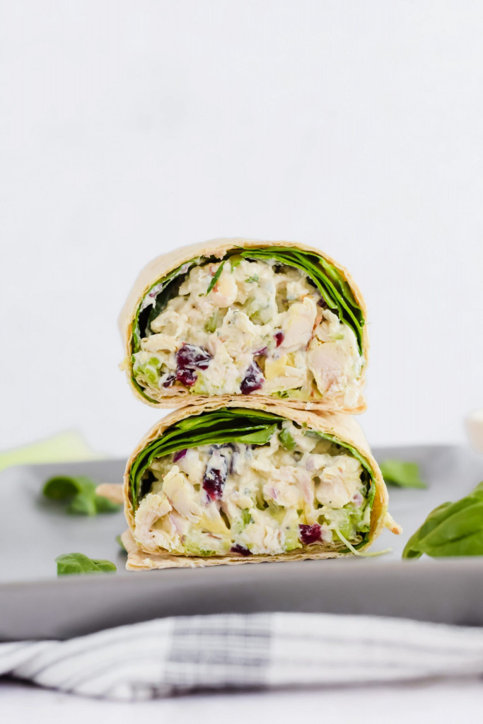 sliced pesto chicken salad wrap halves stacked on top of each other, filled with chicken salad and spinach on gray plate