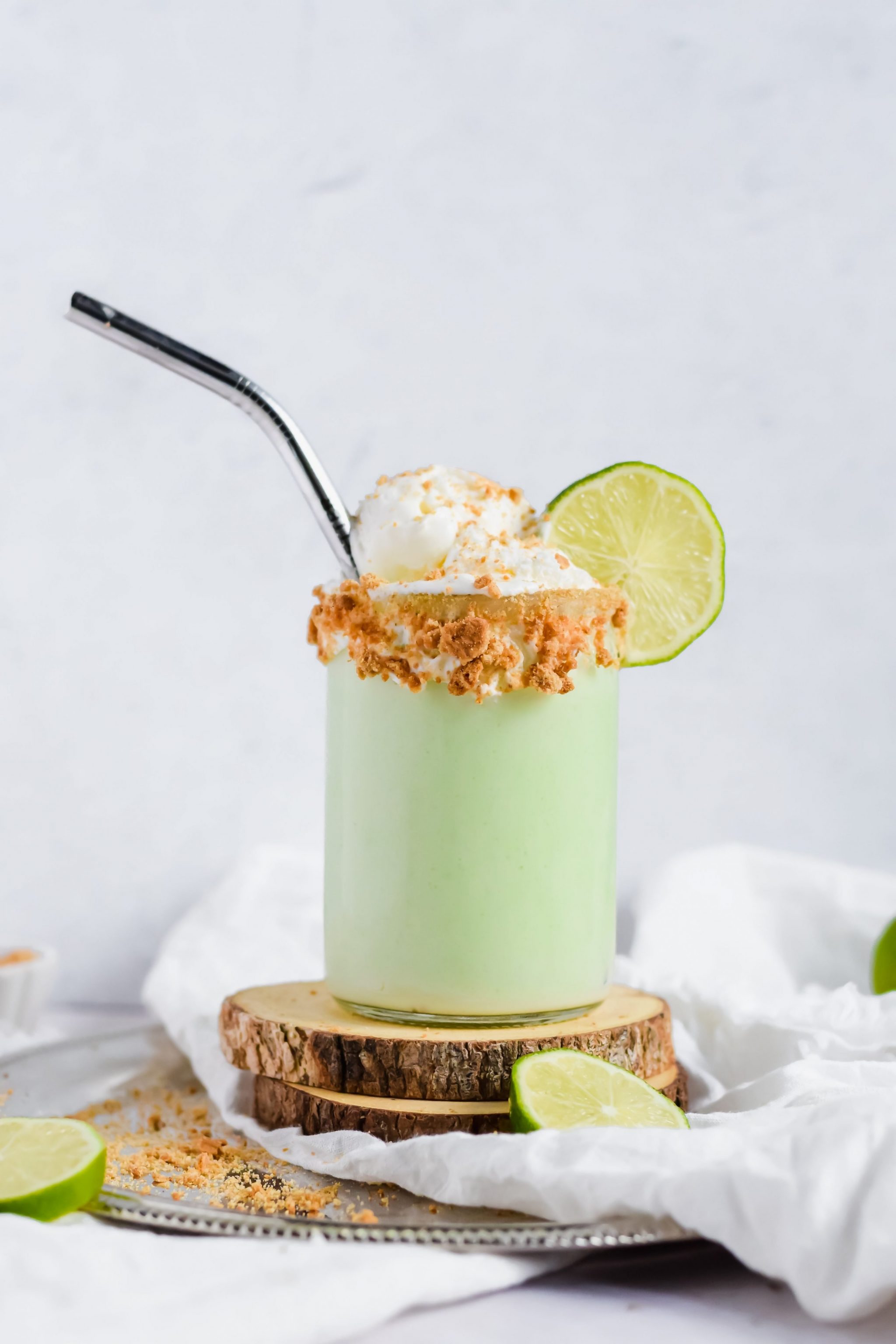 Key Lime Pie Milkshake topped with Cool Whip, crumbled graham cracker and a slice of lime with a metal straw.