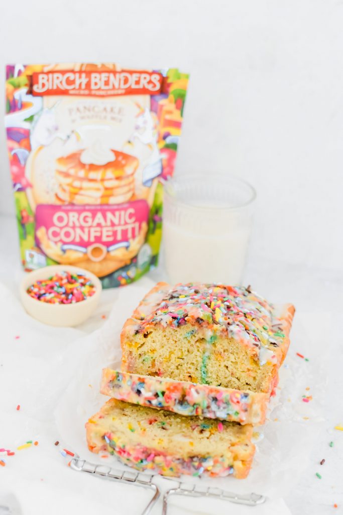 sliced funfetti pancake bread in loaf with glass of milk, sprinkles, and packaging behind