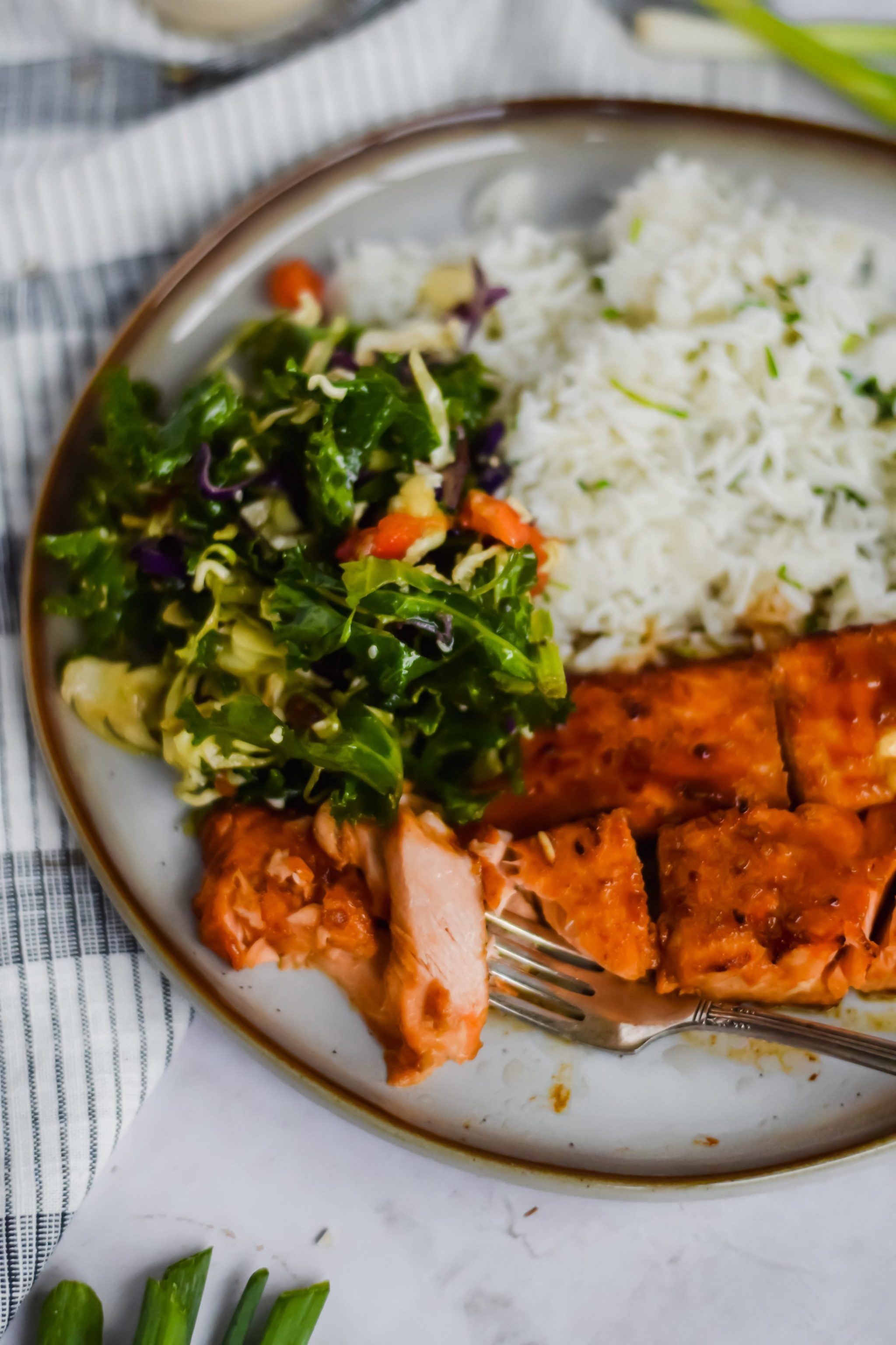 fork cutting grilled teriyaki glazed salmon with slaw salad and rice on the side