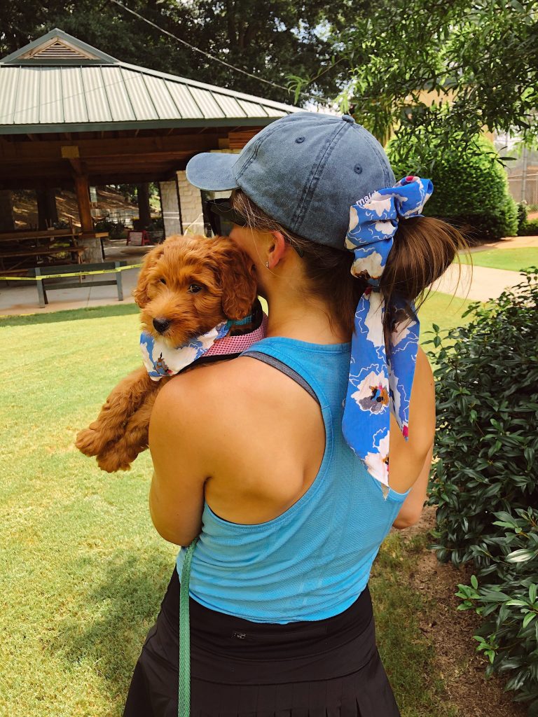 back of girl in tennis outfit holding a small puppy over her shoulder