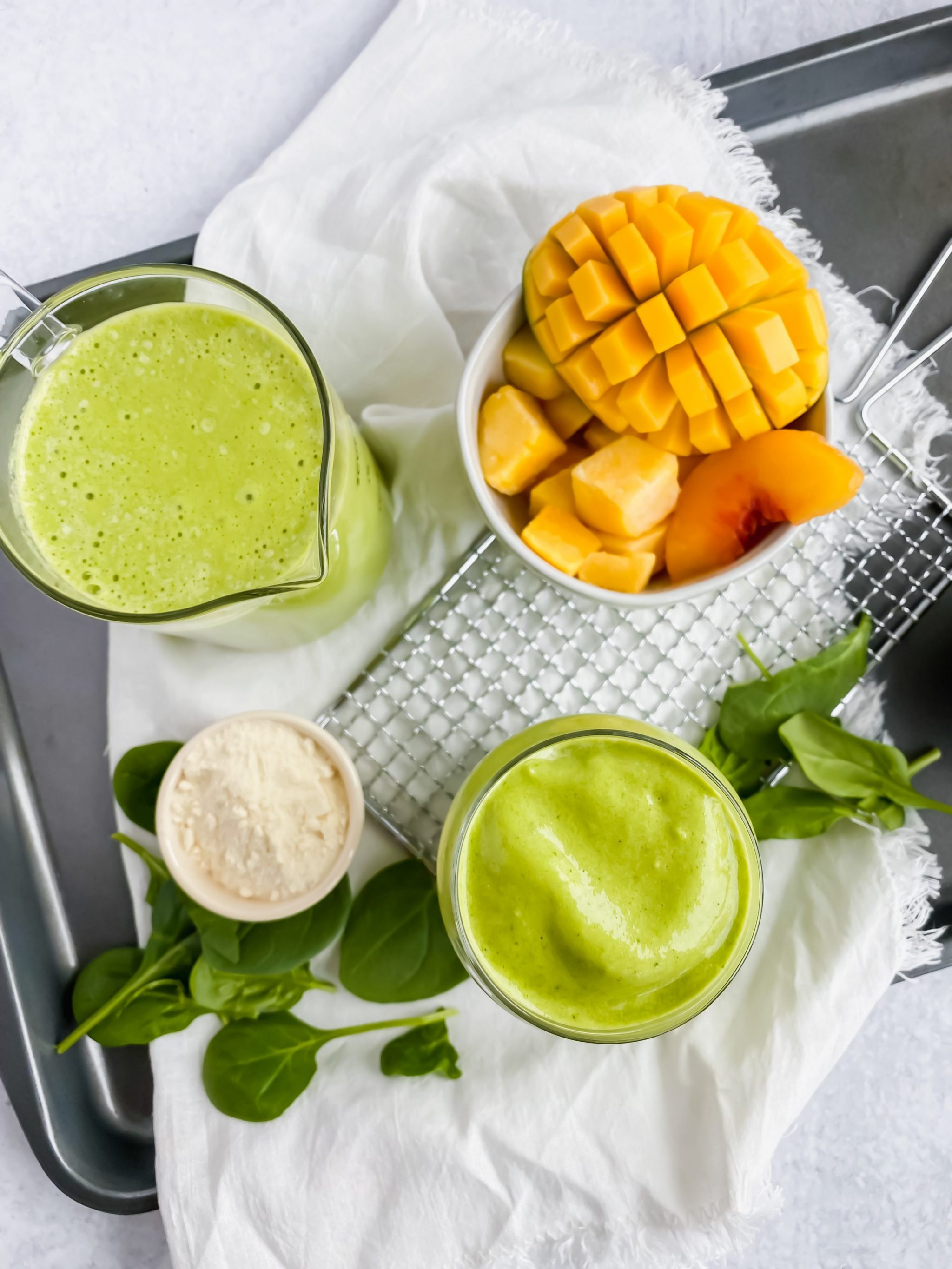 overhead image of two cups filled with green smoothie with frozen mango, spinach, and protein powder on the sides