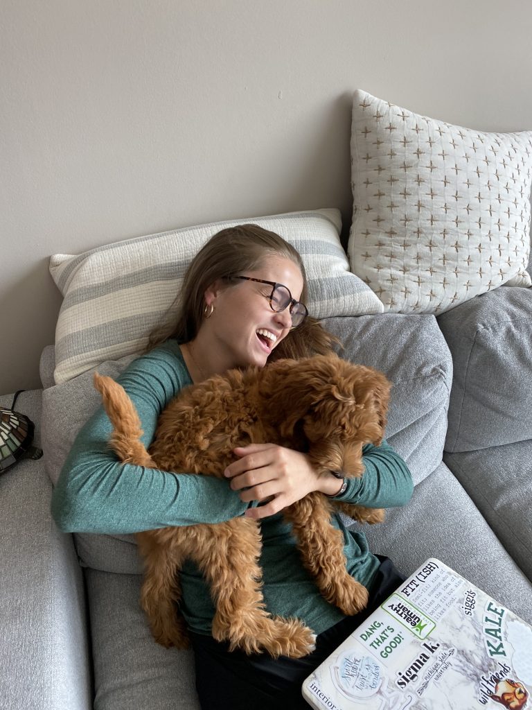girl holding small puppy on sofa while laughing together