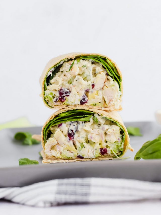 sliced wrap stacked on top of each other, filled with chicken salad and spinach on concrete plate