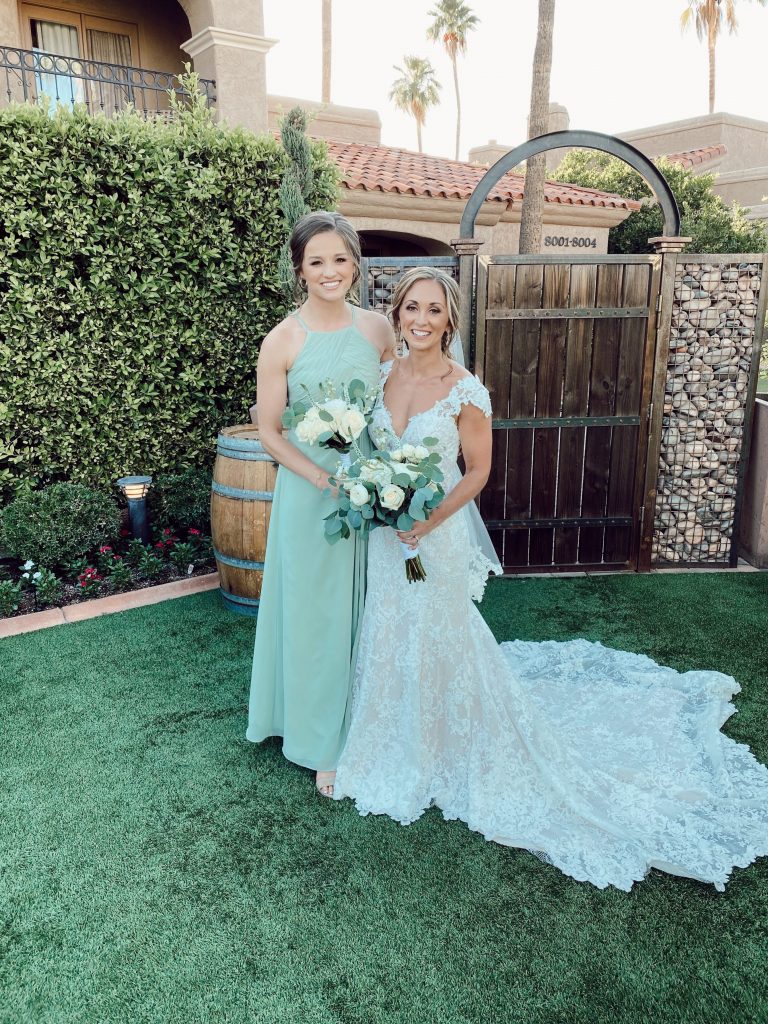 a bride and bridesmaid smiling with their bouquets in front of wooden barn door in Scottsdale