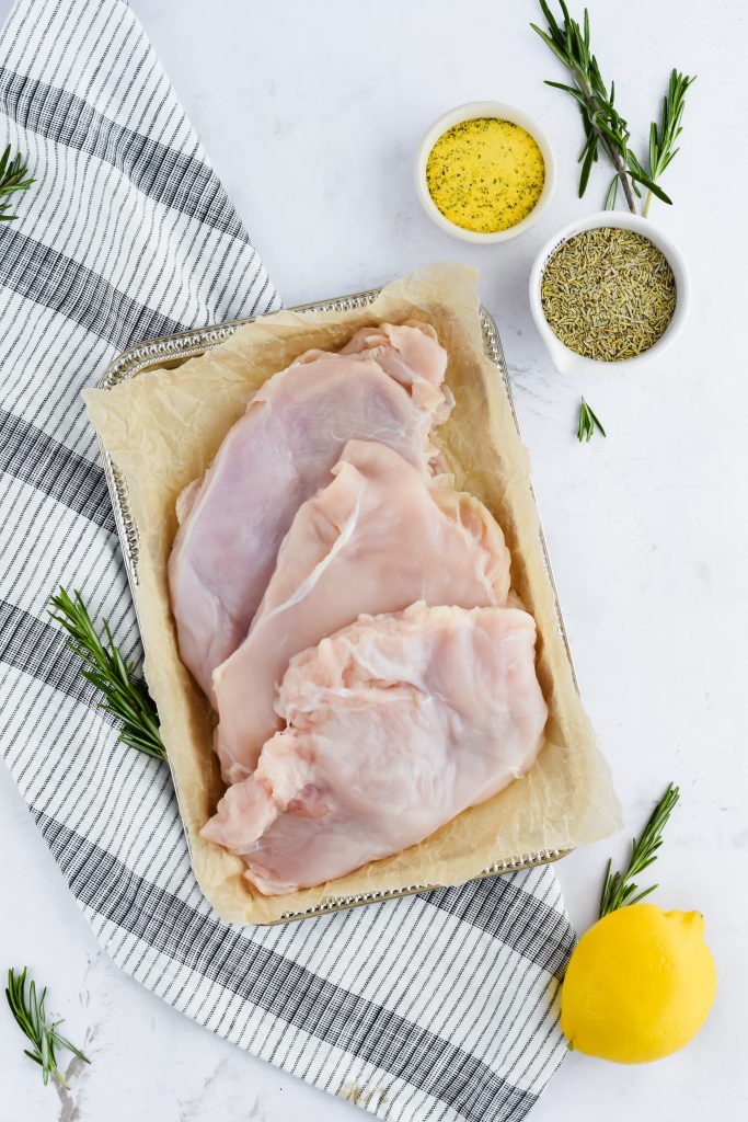 three large chicken breast uncooked on sheet pan with seasonings surround