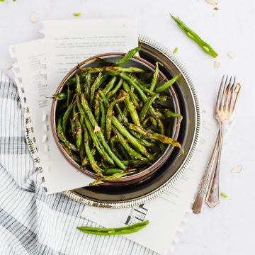 bowl of roasted green beans plated in a black bowl and styled on white background