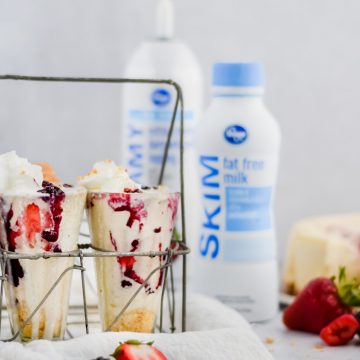 close up of milkshakes filled in glass jars, topped with whip cream and stacked with berries