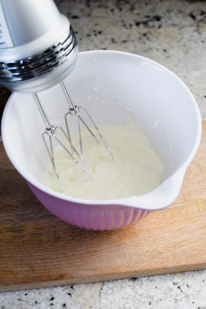 hand mixer in pink bowl with whipped frosting