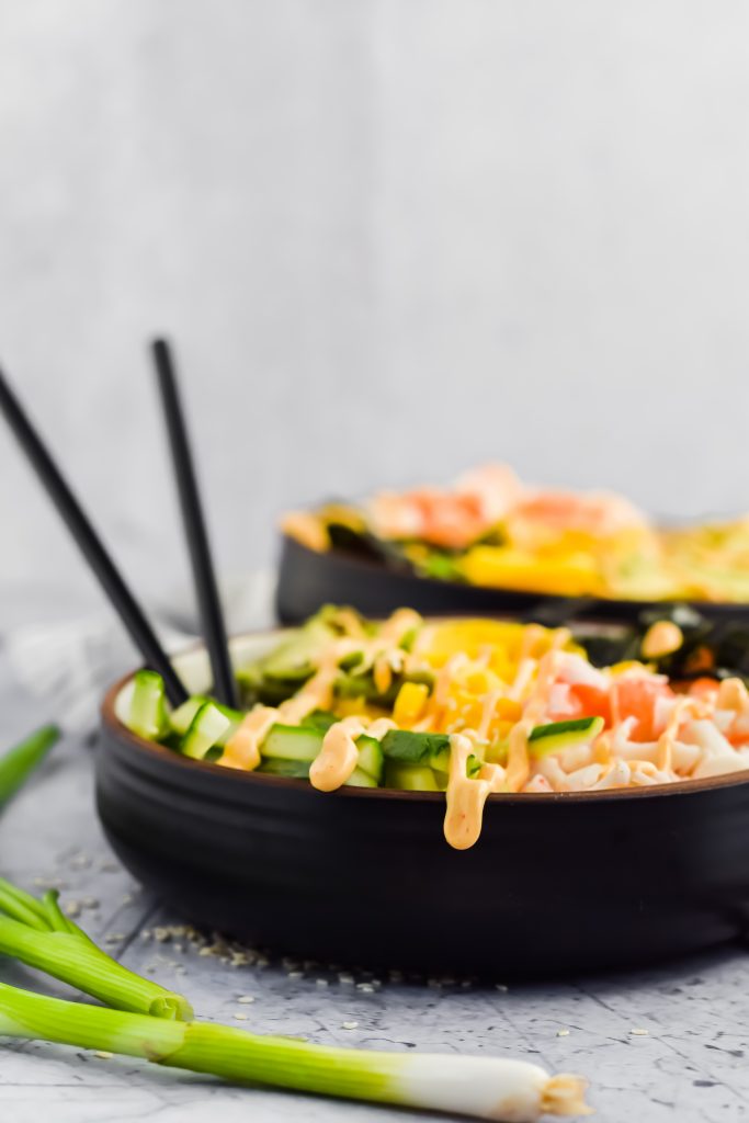 side view of one finished california poke bowl with chopsticks sticking out with additional bowl blurred in background