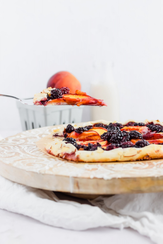 hand holding a pie server with a slice of peach blackberry galette