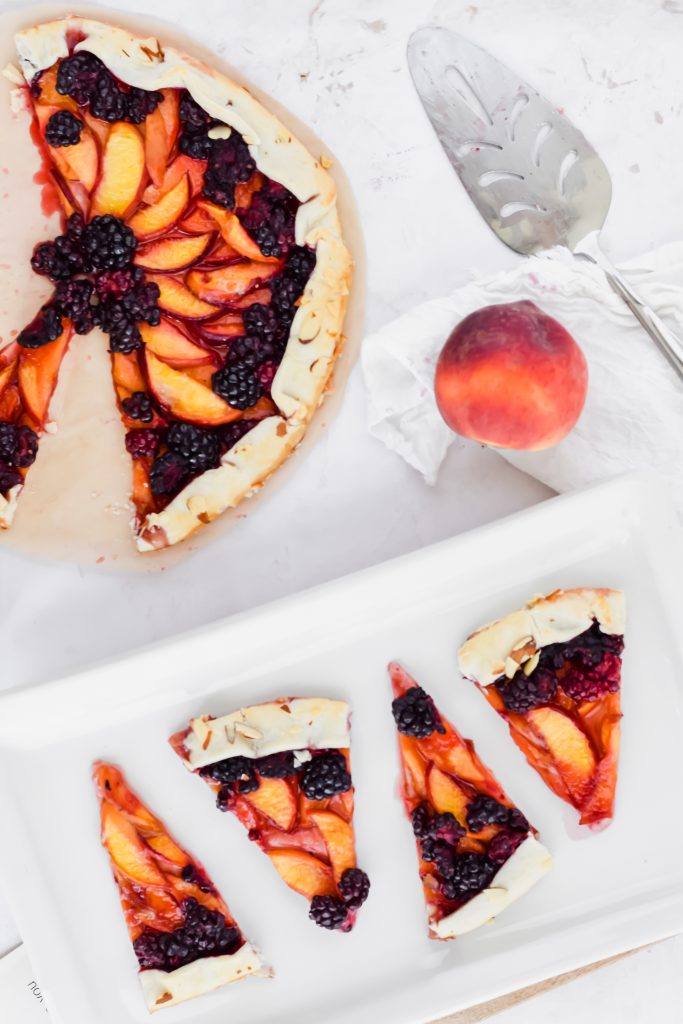 blackberry peach galette plated on white ceramic dish with other pieces surrounding it