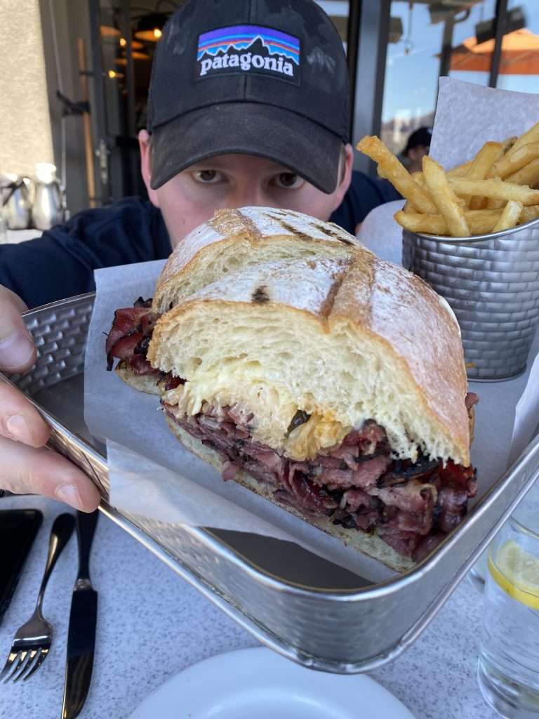 man holding tray of large pastrami reuben sandwich with fries