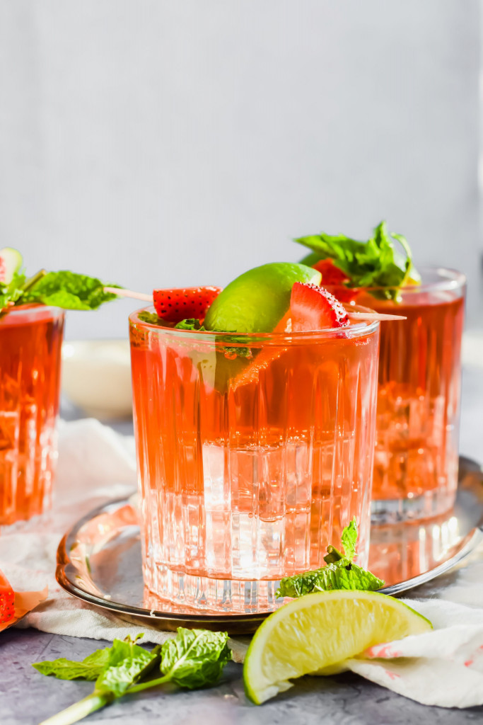 close up filled cocktail glasses with Caribbean Rum Punch topped with fresh mint, strawberries, and lime