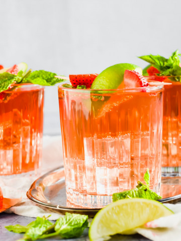 close up of cocktail filled with ice and rum punch and garnished with strawberries and lime