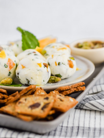 90 degree image of dried mango goat cheese balls on a platter with mint and crackers garnished around it