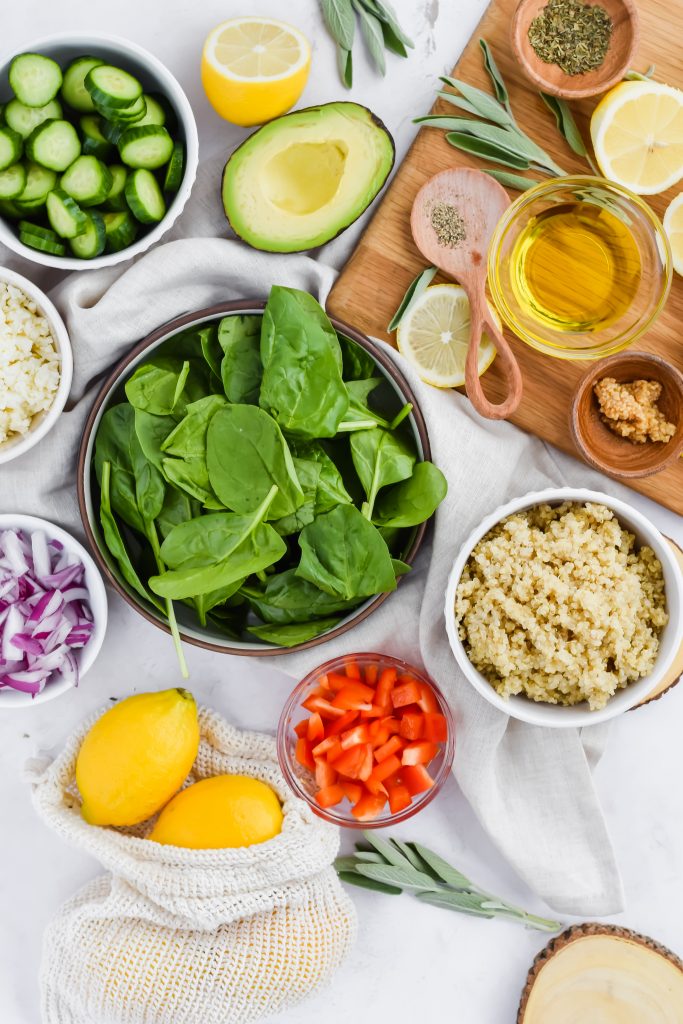 ingredients needed for spinach quinoa salad in separate bowls on white background