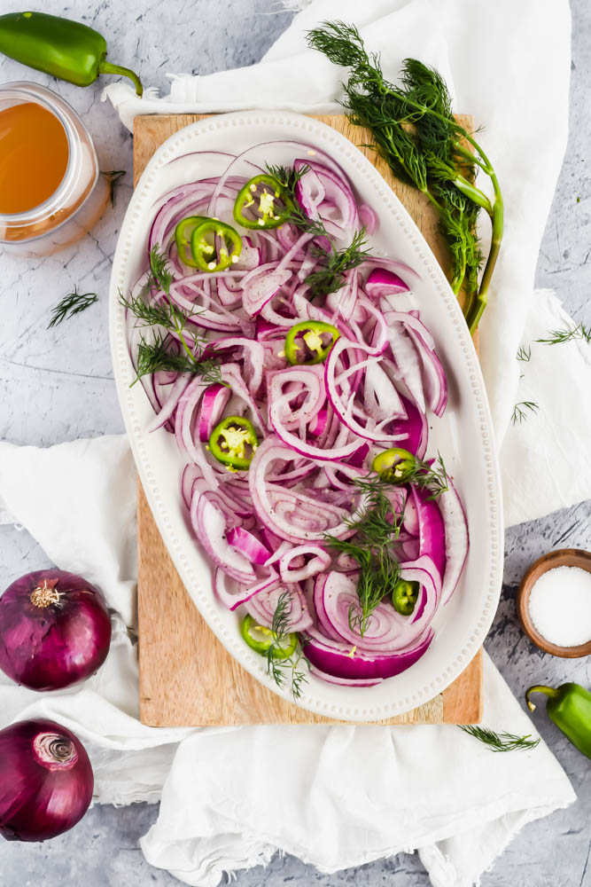 white platter filled with red onions sliced and garnished with dill