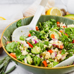 tossed spinach quinoa salad loaded with veggies in green salad bowl and white ceramic tongs