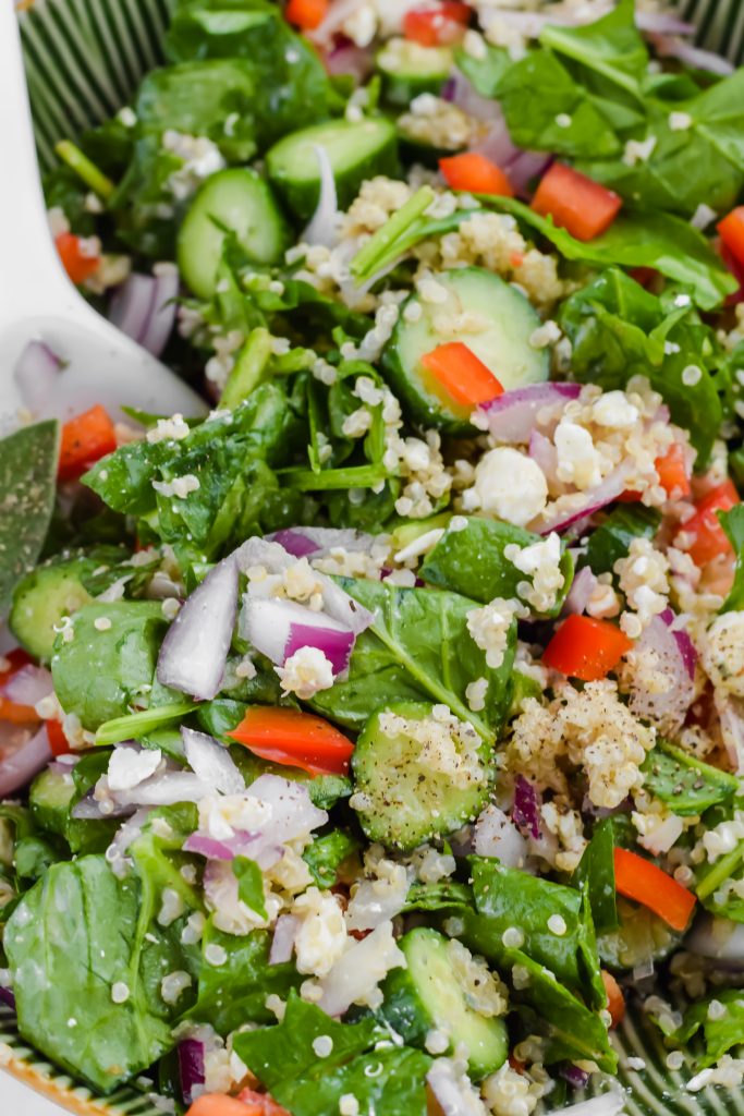 very close up image of tossed salad and dressed with focus on cucumbers, quinoa, and red pepper