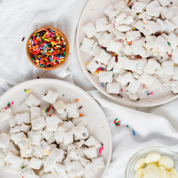 two plates of funfetti puppy chow plated on white dishes and sprinkles surrounding them