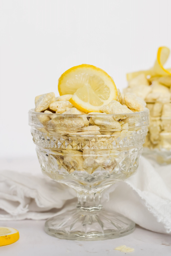 close up image of lemon puppy chow in glass container topped with slice of lemon