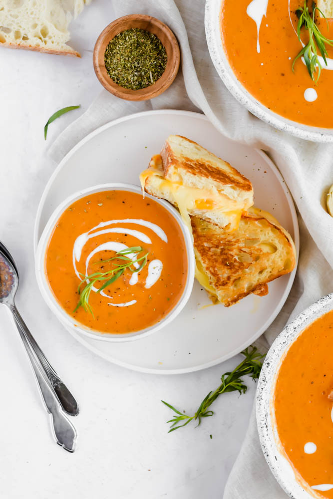bowl of dairy free tomato soup with two pieces of grilled cheese aside it.