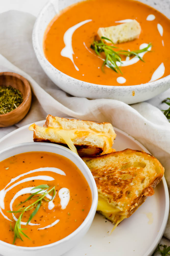 bowl of dairy free tomato soup with two pieces of grilled cheese aside it.