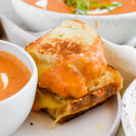 stacked grilled cheese sandwich dunked in roasted tomato soup on white plate.