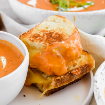 stacked grilled cheese sandwich dunked in roasted tomato soup on white plate
