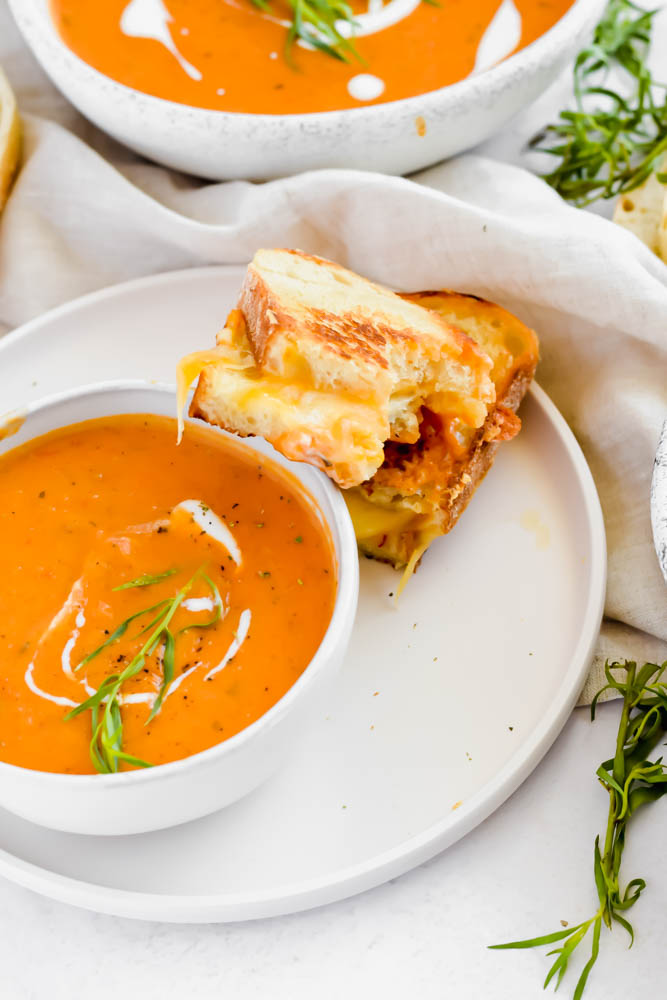 bowl of tomato soup with two pieces of grilled cheese aside it