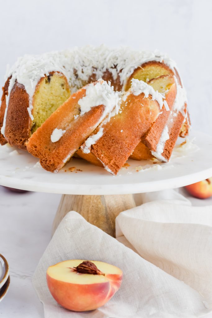 sliced peach pound cake on white marble platter with fresh peaches on the side