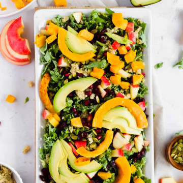 rectangular platter filled with kale butternut squash and fruit salad garnished with avocado and dried cranberries