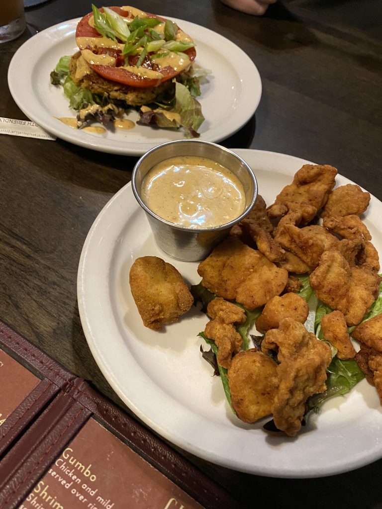 two white plates with crab cakes and fried alligator appetizers on them