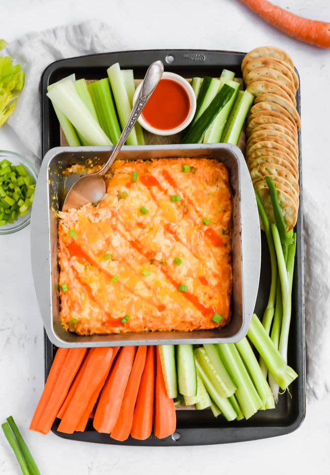 tray full of buffalo chicken dip plated with colorful vegetables and crackers