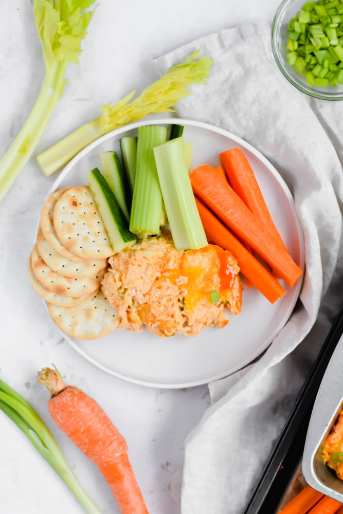 white snack plate with fresh celery, carrots, crackers and buffalo chicken dip on platter