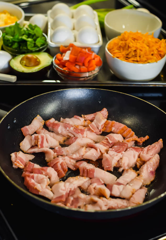 close up of uncooked bacon in a frying pan and other ingredients in the background