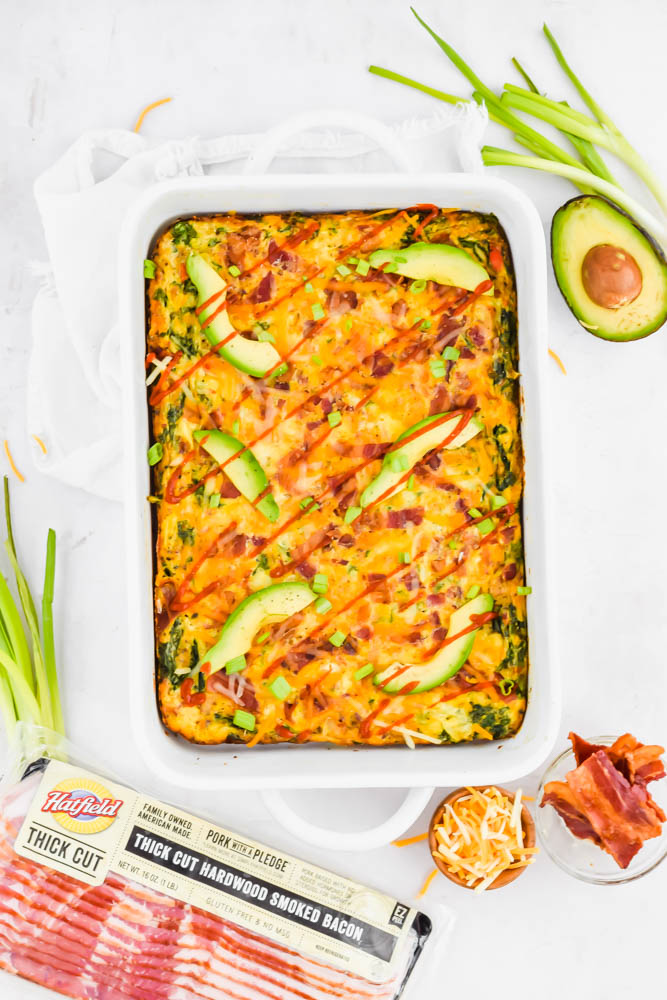baked bacon sweet potato and egg casserole topped with sliced avocado and sriracha drizzle