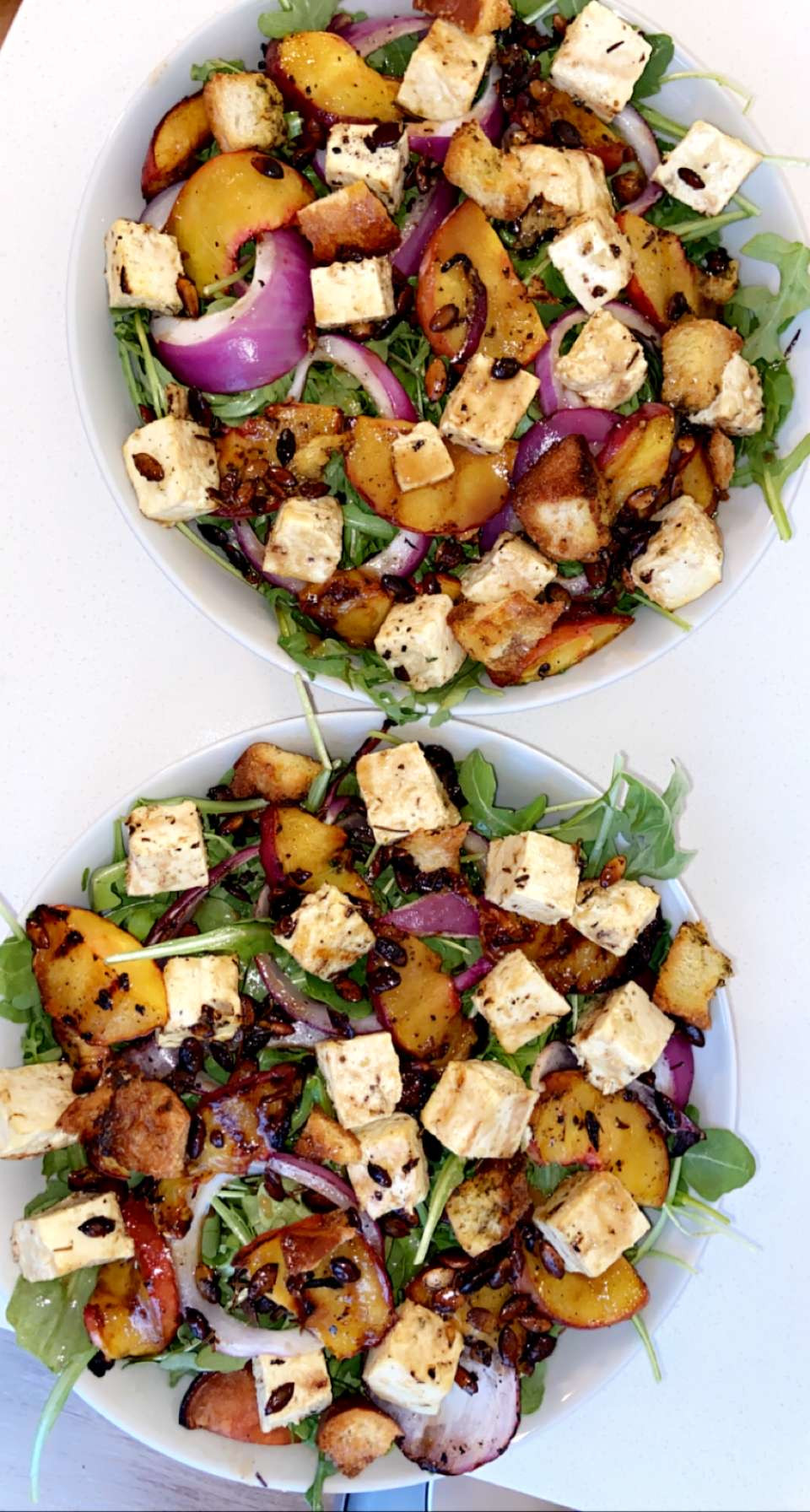 two bowls of salad topped with caramelized onions, peaches, balsamic dressing and feta cheese