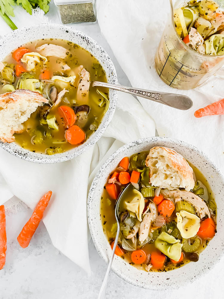 two bowls of chicken tortellini soup loaded with carrots and celery topped with a baguette