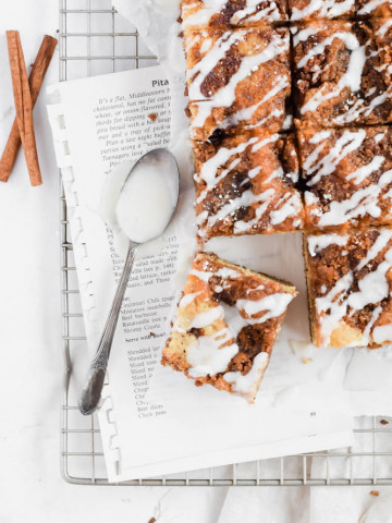 sliced cinnamon streusel coffee cake drizzled in icing on parchment paper.