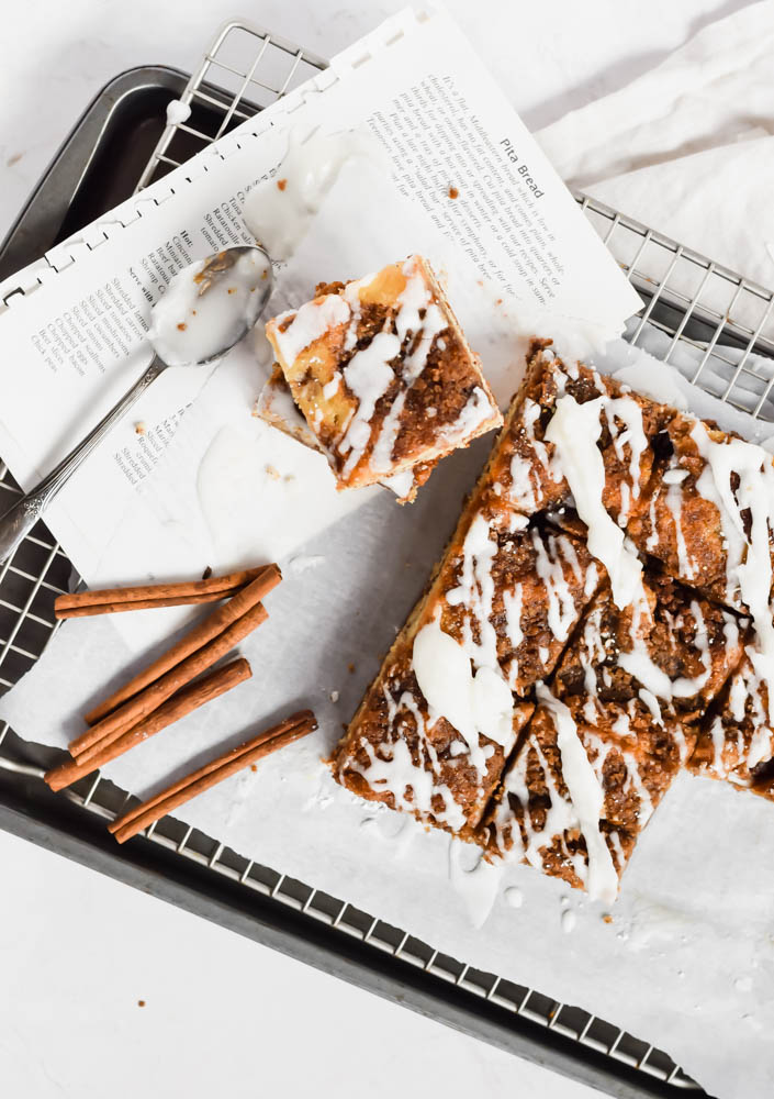 cinnamon crumble coffee cake cut in squares and garnished with cinnamon sticks on a wire rack