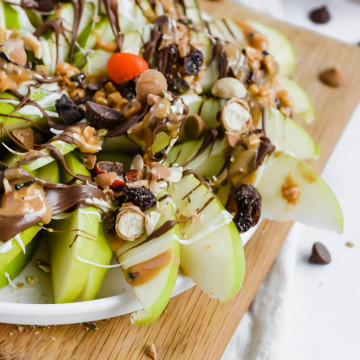 wooden board filled with green apples that are layered in peanut butter, chocolate, white chocolate, and trail mix