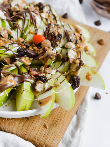 wooden board filled with green apples that are layered in peanut butter, chocolate, white chocolate, and trail mix
