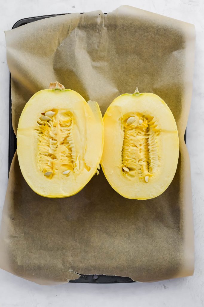 halved spaghetti squash face up on parchment lined baking tray