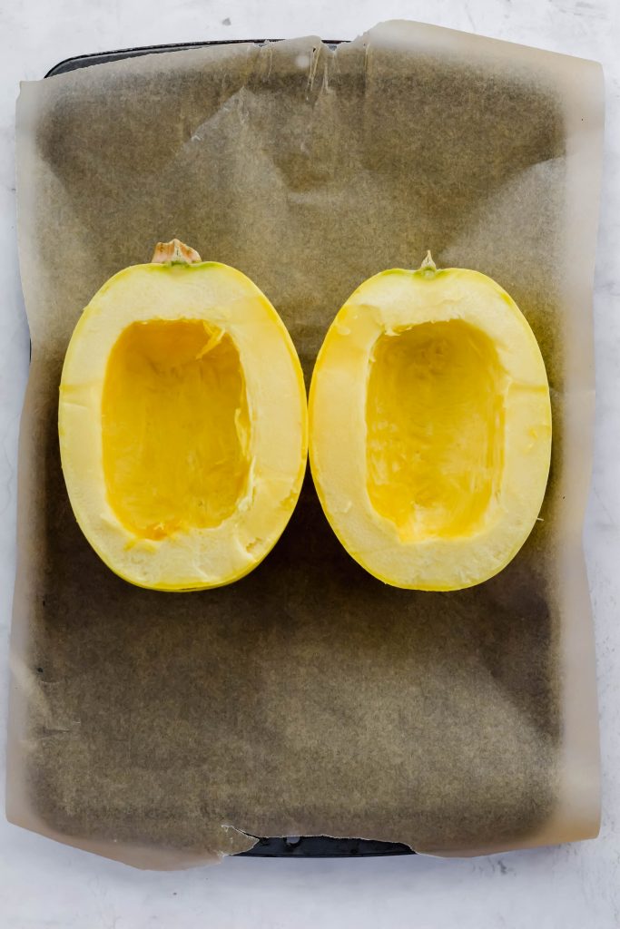 halved spaghetti squash face up on parchment lined baking tray with seeds removed